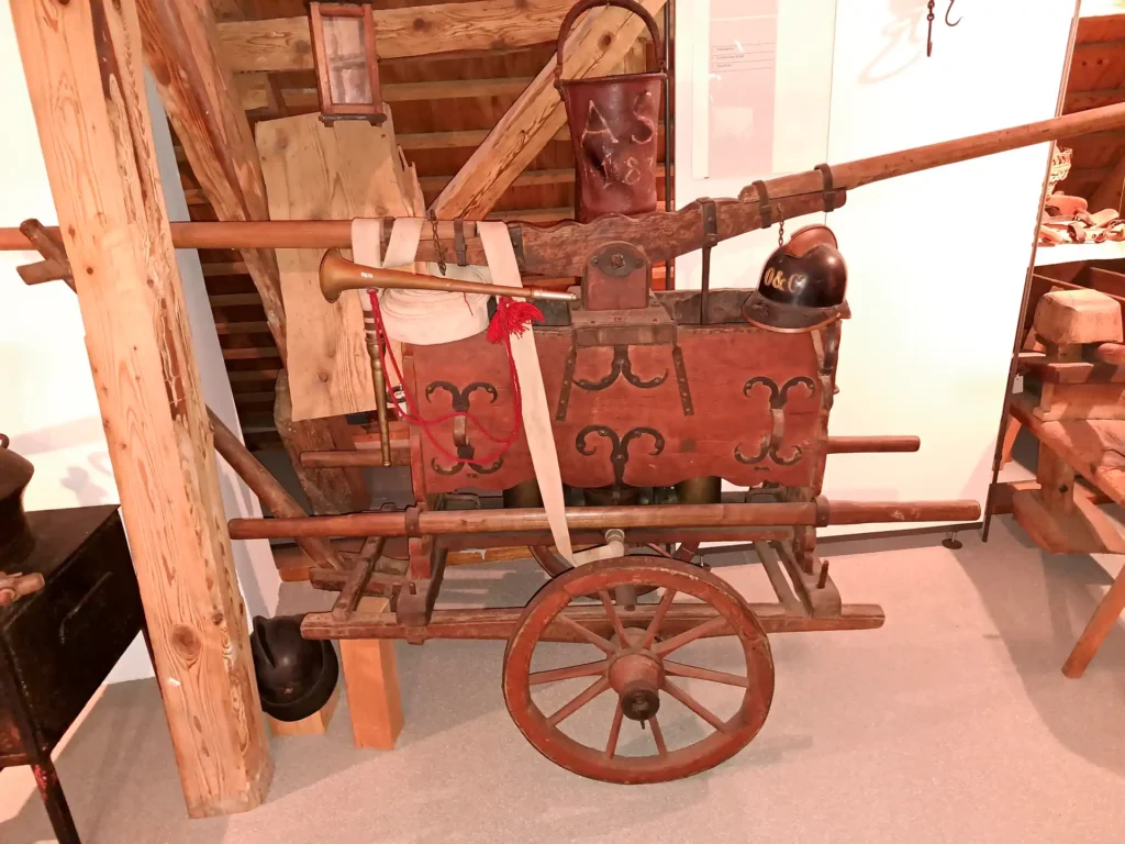 Zu sehen ist eine alte Feuerspritze, Schöpfspritze wie sie früher benutzt wurde, um das Wasser von einem Bach zum Brand zu leiten.