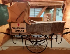Historischer Samariterwagen des Samaritervereins Gränichen mit geflochtenem Wagenkasten, Stoffverdeck und rotem Kreuz. Ausgestellt im Museum Chornhuus.